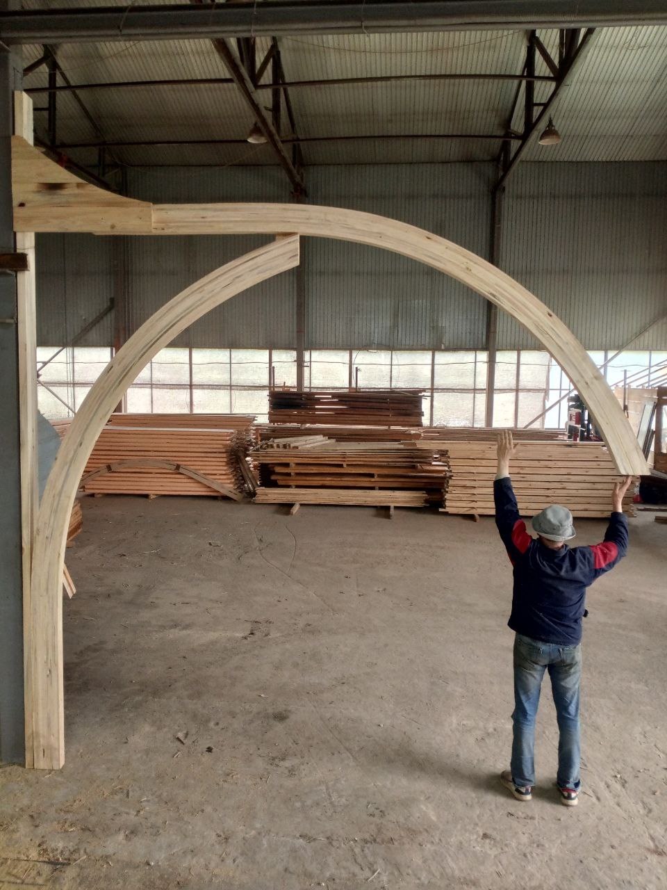 Клеєна стрільчаста арка GoodWoodHome у зборі в цеху — людина з піднятими руками для масштабу